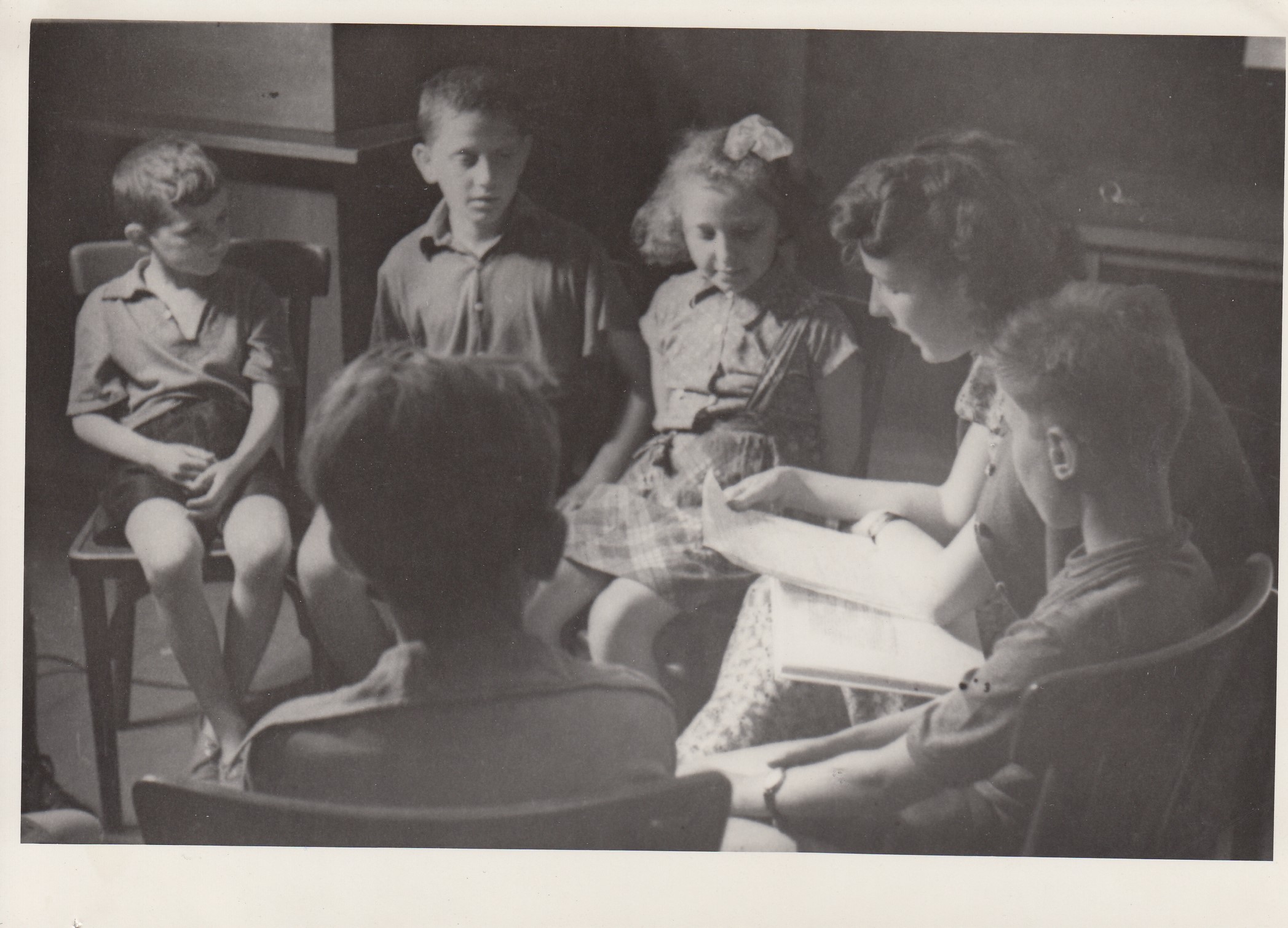 Na fotke zo šesťdesiatych rokov žena predčíta skupinke detí.